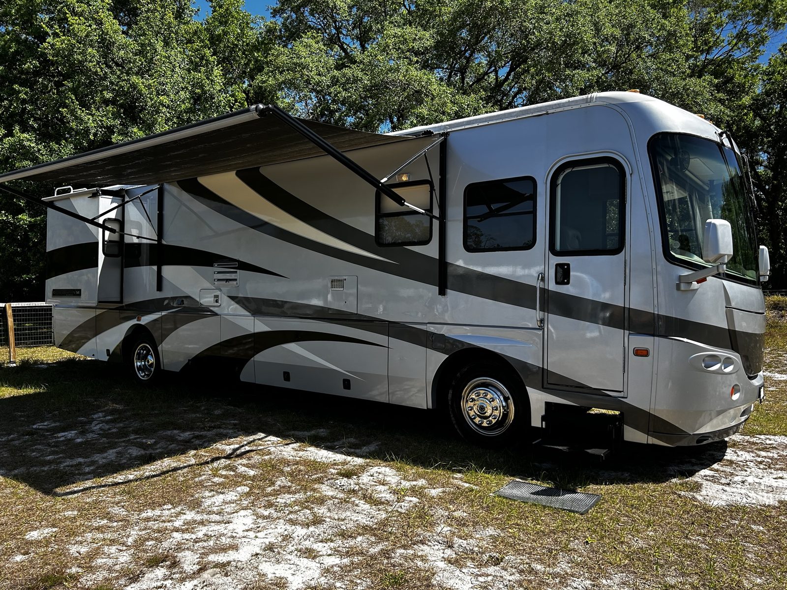 Class A diesel motorhome with awning extended at a wooded storage lot